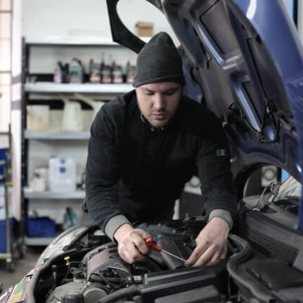 Certified auto body mechanic at IQ Collision Center performing precision engine bay repairs and vehicle maintenance.